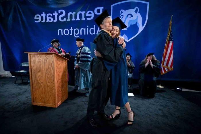 student and professor hugging on commencement stage